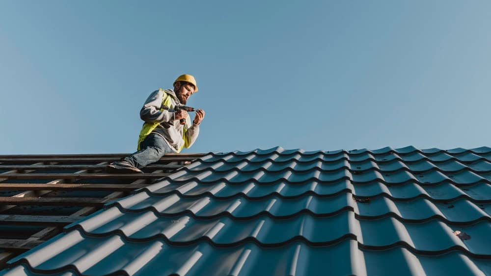 Roofing expert inspecting a blue metal roof in New Jersey for potential replacement needs.
