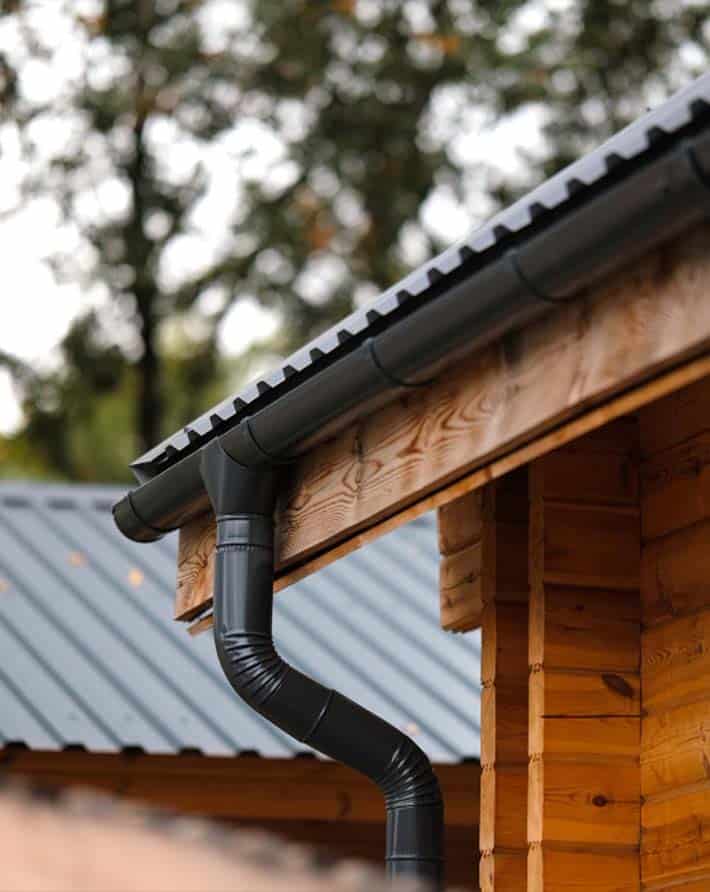 Gutter system installed on a wooden house with black downspouts and roof edge.