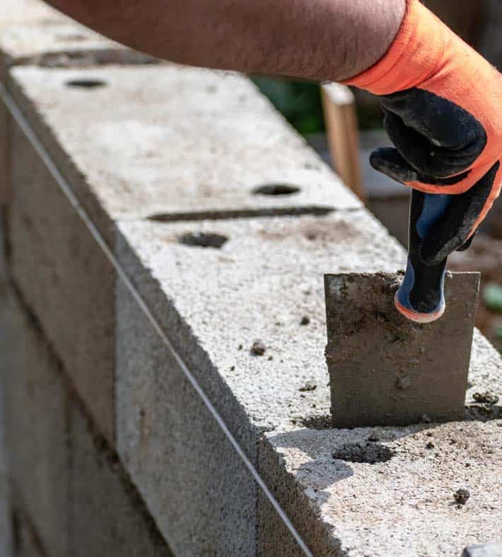 Masonry worker laying concrete blocks for roofing or siding project.
