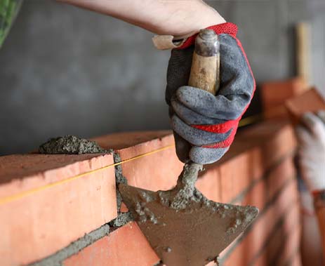 Masonry worker applying mortar to bricks with a trowel for building or repair.