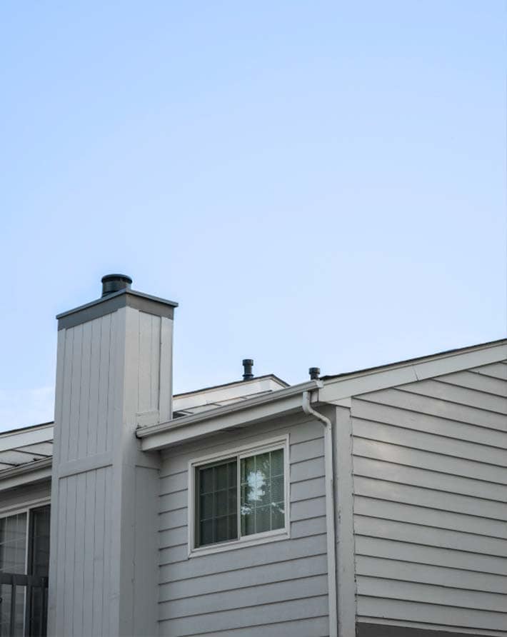 Close-up of new siding on a house with a chimney and window.