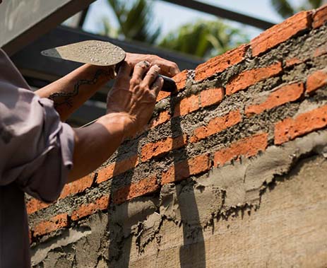Masonry wall being built with bricks and mortar by a worker.