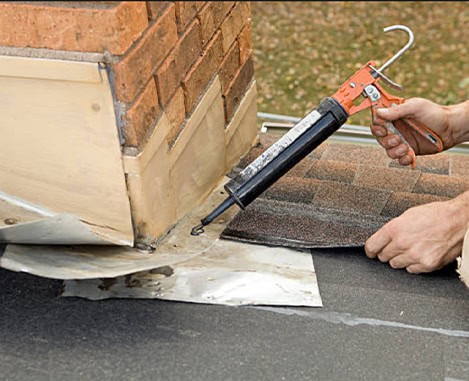 Chimney repair sealant applied with caulking gun around brick chimney on asphalt roof.