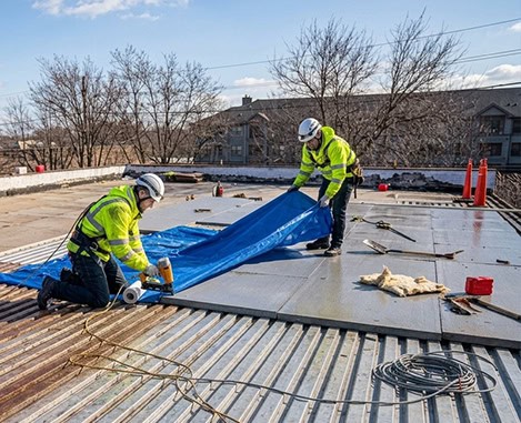 BlueSky Roofing crew on a flat roof unrolling a blue tarp for roof replacement