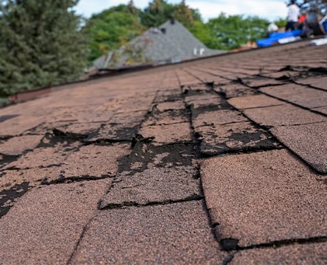 Damaged asphalt shingle roof on a residential home; roof replacement with workers in Clifton NJ
