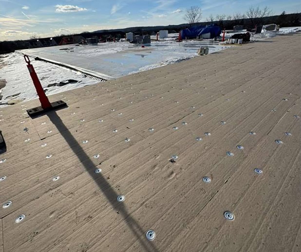 Flat roof with numerous fasteners on beige membrane for roof replacement in New Jersey