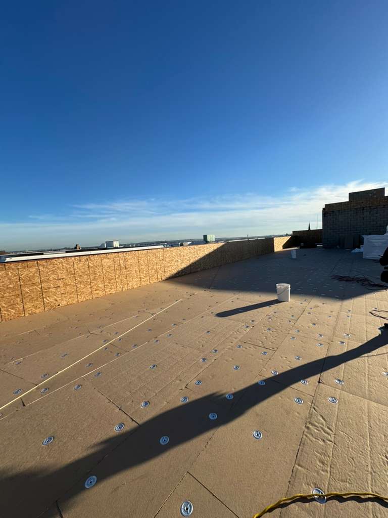 New Jersey roof installation on a flat roof showing beige underlayment, numerous screws, under a clear blue sky.