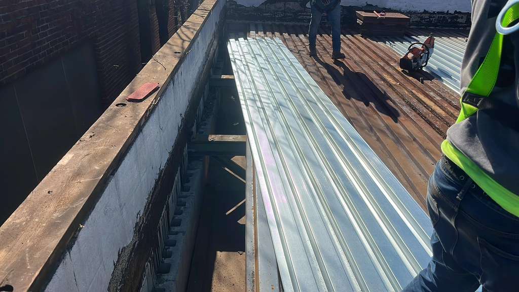 Roof replacement underway: shiny metal roof panels installed on a flat roof; workers on-site.