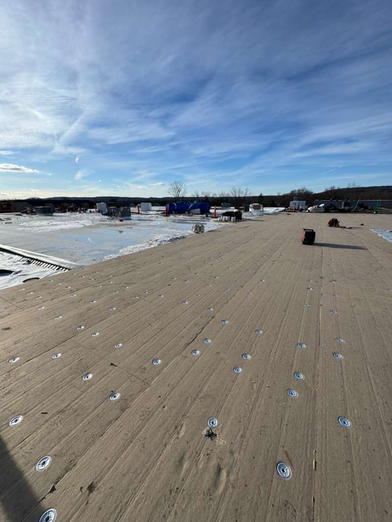 Beige flat roof with numerous screws for roof replacement, construction site in background.