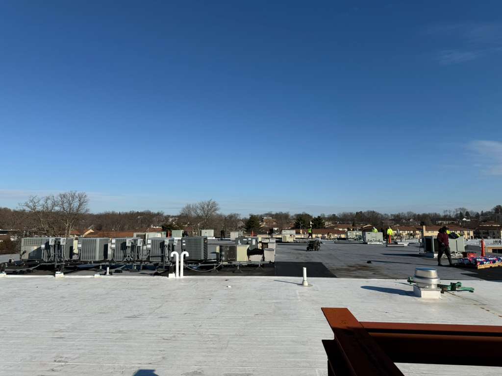 Flat commercial roof with multiple HVAC units and workers in the distance.