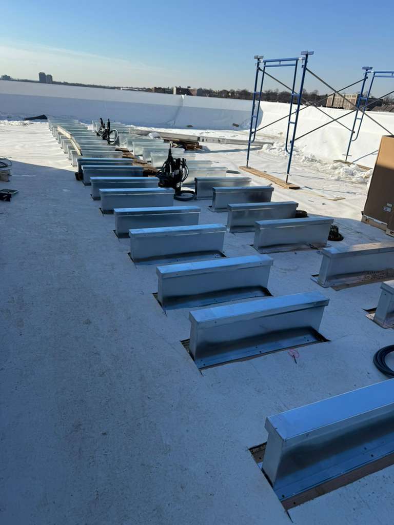 BlueSky roofing crew installing metal roof curbs on a flat, snow-covered roof in New Jersey