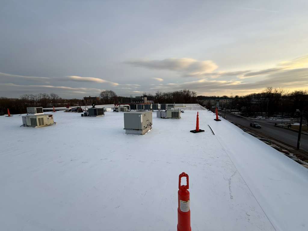 Snow-covered flat roof with HVAC units and orange safety cones for roof leak repair.