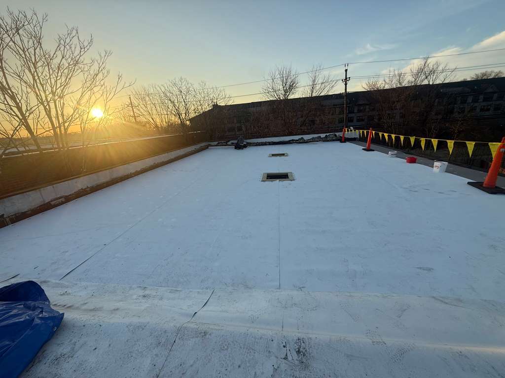 Flat white roof membrane with safety cones and pennant banners at sunset in Clifton NJ
