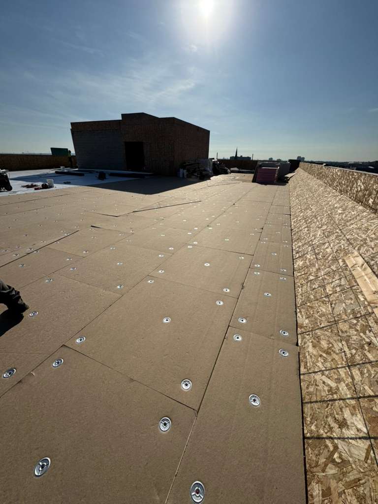 Flat roof with brown underlayment panels and exposed screws for roof replacement