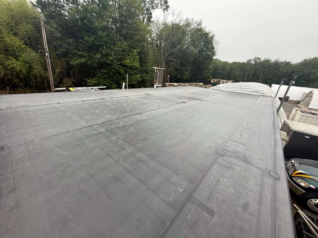Flat gray roofing membrane on a large roof; trees in background.