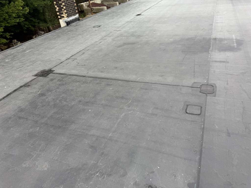 Flat gray roof with seam lines and two roof hatches.