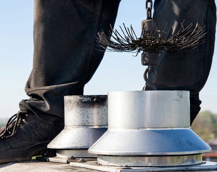 Close-up of metal roof vent caps and a hanging wire brush with booted legs visible.