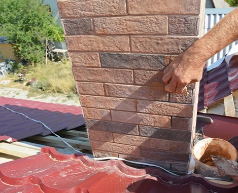 Hand applying mortar during masonry work on brick chimney on a red metal roof in Clifton NJ