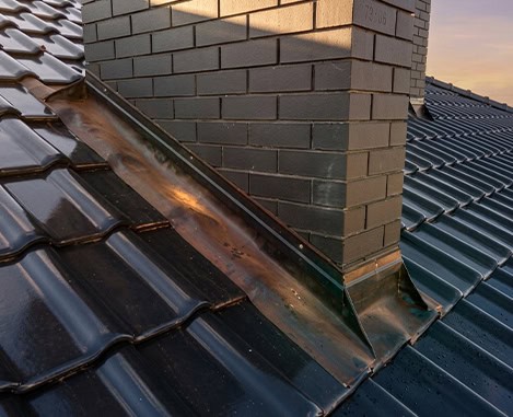 Brick chimney with copper flashing on a dark metal roof, chimney repair in New Jersey