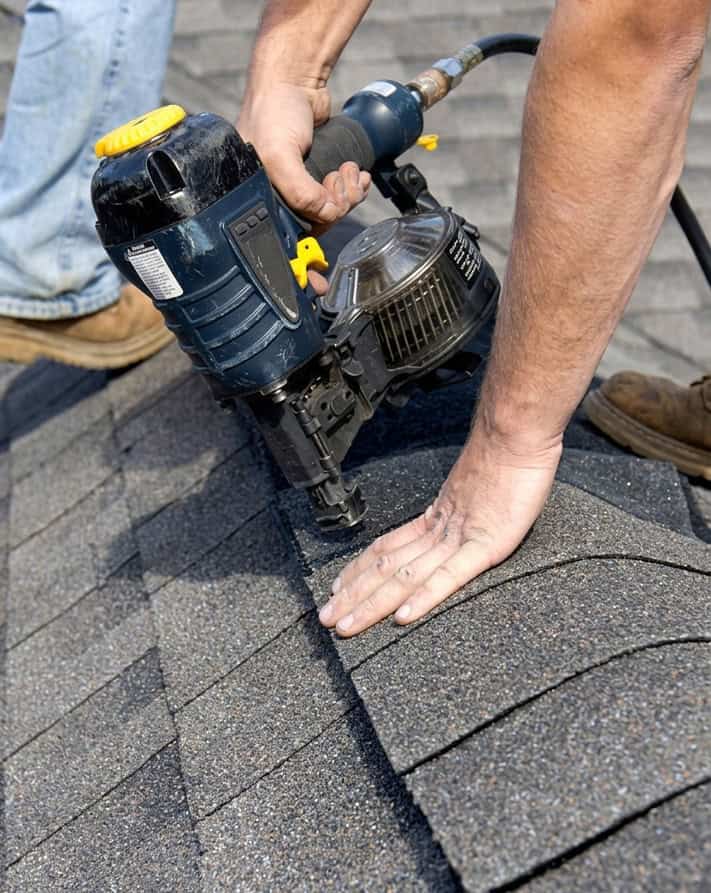 BlueSky roofing crew using a nail gun on asphalt shingles during roof replacement