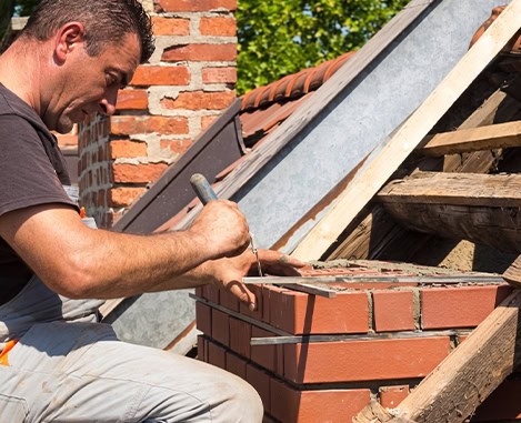 Masonry work: worker trowels mortar on brick chimney beside a roof under construction.