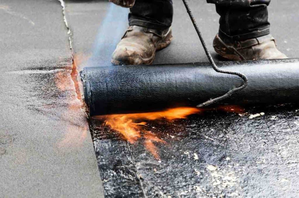 BlueSky roofing crew applying black roof replacement membrane with a torch on a flat roof