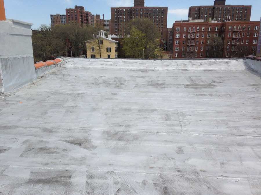 Flat white roof membrane with slight staining and parapet walls, urban brick buildings in distance.