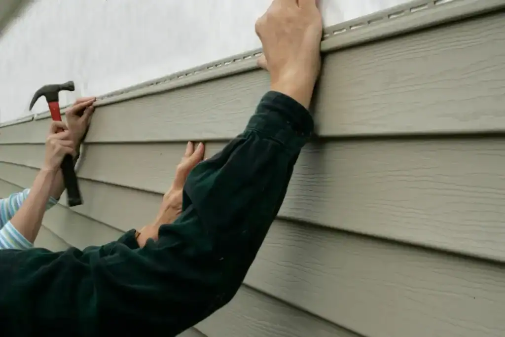 Worker performing siding installation with hammer on beige exterior wall in New Jersey