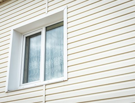 Beige vinyl siding with a white-framed window; siding installation in New Jersey.
