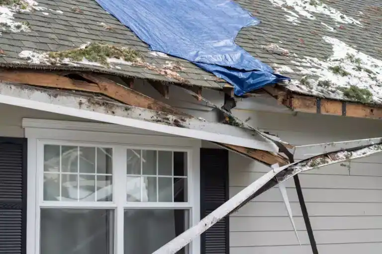 Damaged asphalt roof with torn decking and blue tarp, exposed wooden beams, emergency roofing in Clifton NJ.