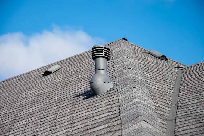 Gray asphalt shingle roof with a metal vent pipe against a blue sky.