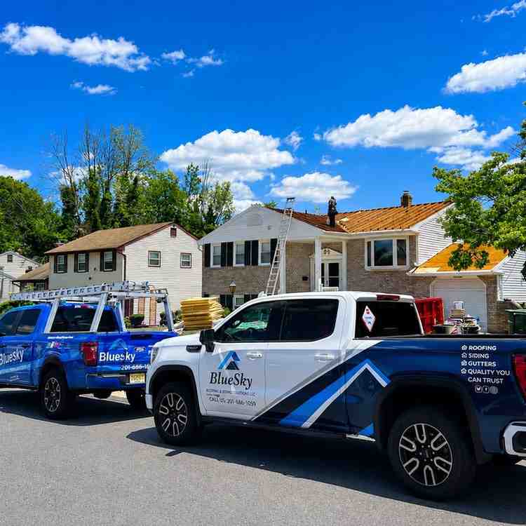 BlueSky Roofing & Siding trucks parked in front of a New Jersey home with a ladder on the roof.
