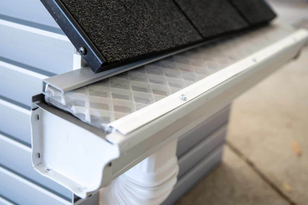 White gutter installation with mesh screen along blue siding under roof shingles