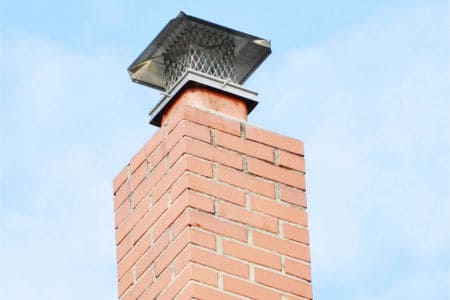 Brick chimney with metal cap against a blue sky