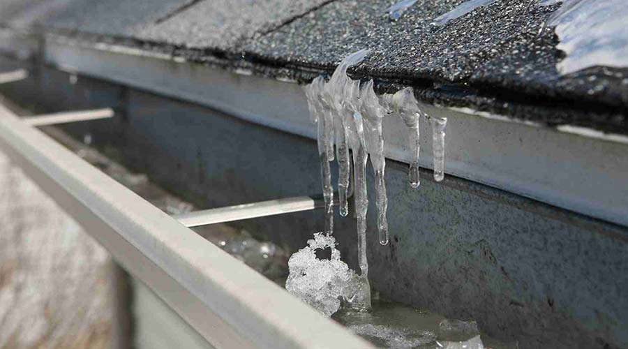 Ice dam forming on roof edge with icicles and melting snow.