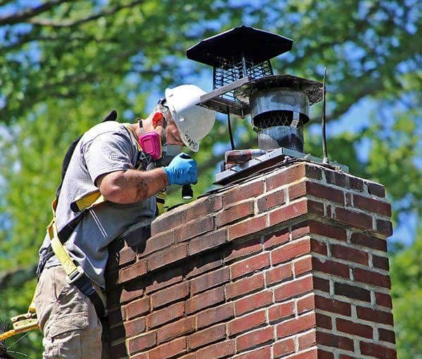 Roofing contractor inspecting a brick chimney crown for cracks and water damage in Morristown, NJ.